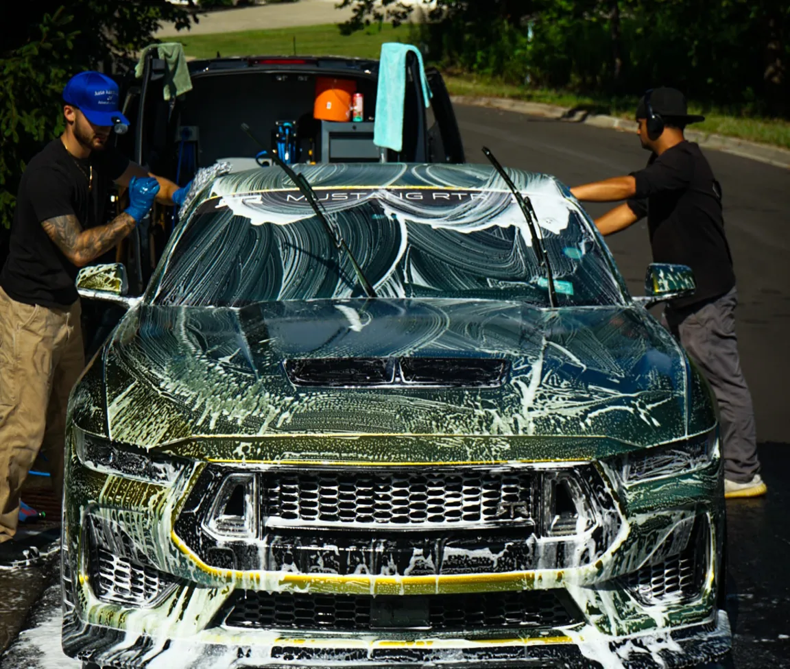 The Auto Aesthetics crew foam washing a Ford Mustang in a driveway near Binghamton, NY, with the mobile detailing van behind them