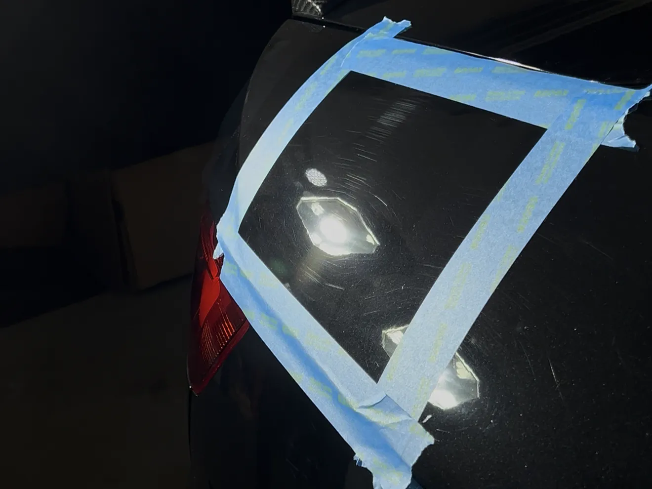 A taped off test section on a black trunk lid showing swirl marks under inspection lights before paint correction by Auto Aesthetics near Binghamton, NY